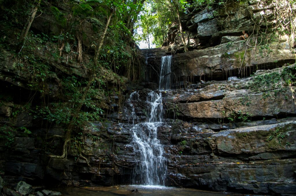 A tranquil waterfall cascading down rocky cliffs surrounded by lush jungle greenery in Kampot, Cambodia.