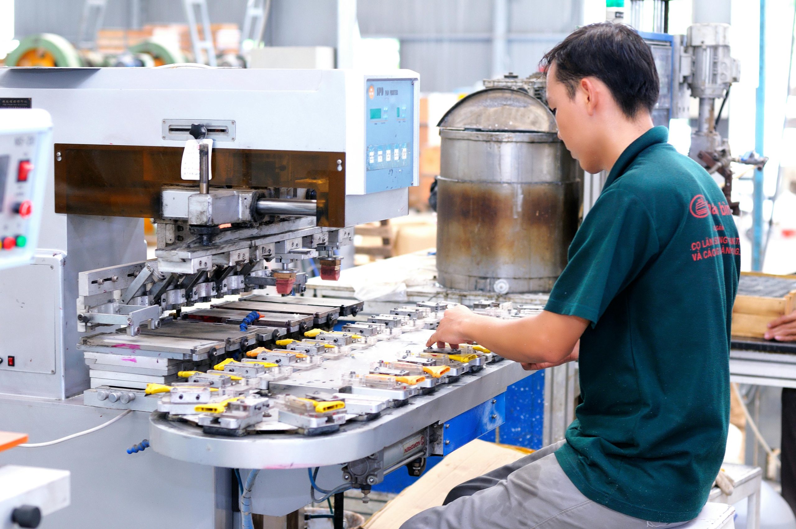 Asian male worker focused on operating machinery in a modern factory setting.
