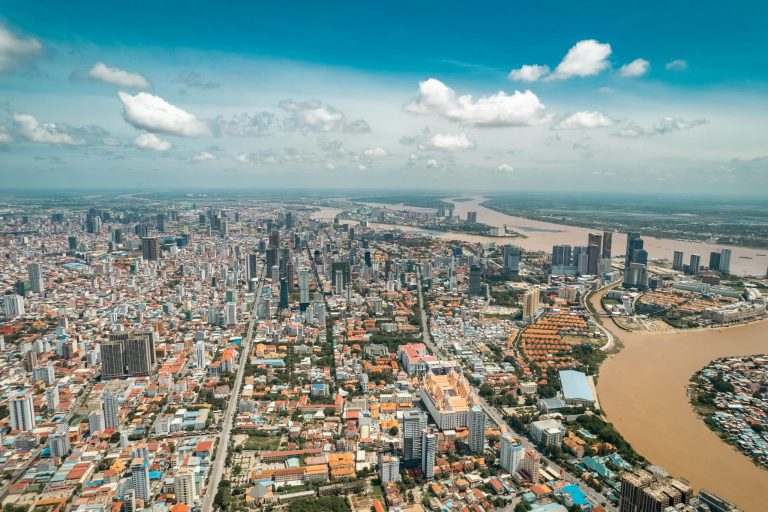 Stunning aerial view of Phnom Penh's skyline along the river under a blue sky.